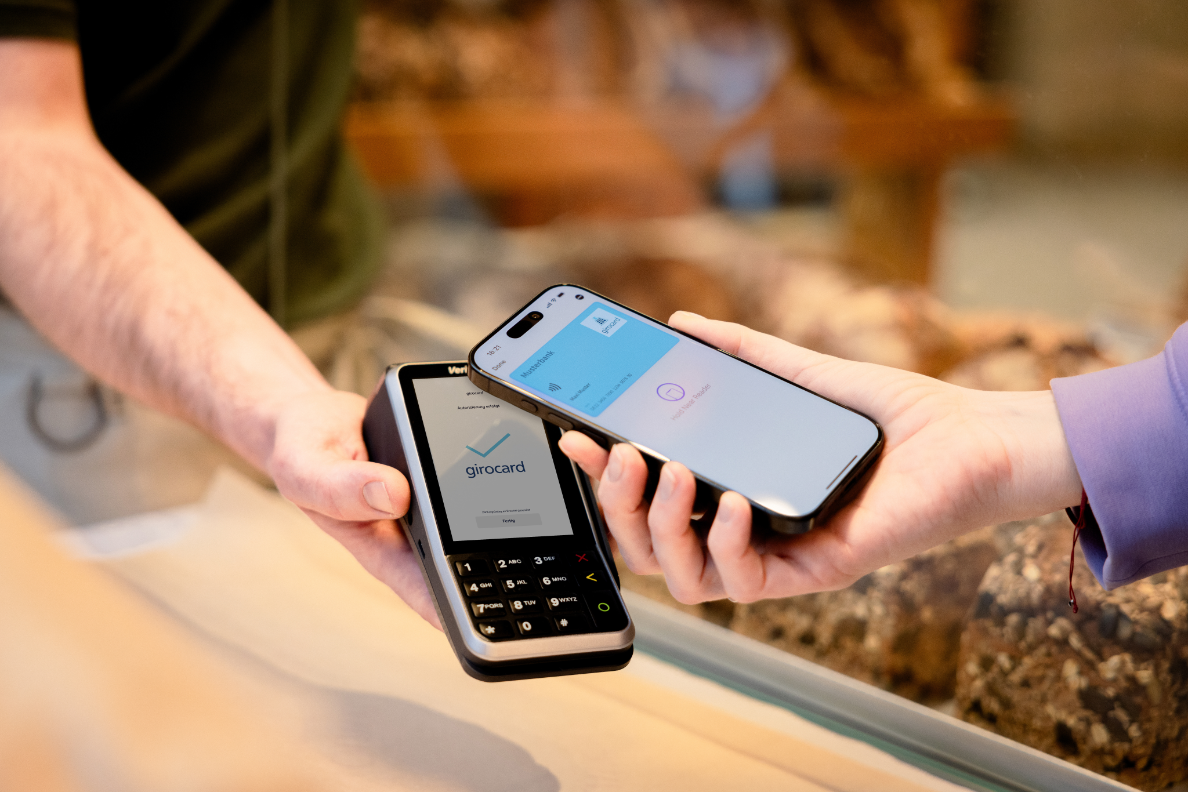 Zahlungsvorgang im Geschäft, bei dem eine girocard an ein Kartenterminal gehalten wird, während ein Smartphone zur kontaktlosen Bezahlung genutzt wird. Erzielt eine moderne Zahlungsmethode durch die Kombination von Hardware und mobiler App.